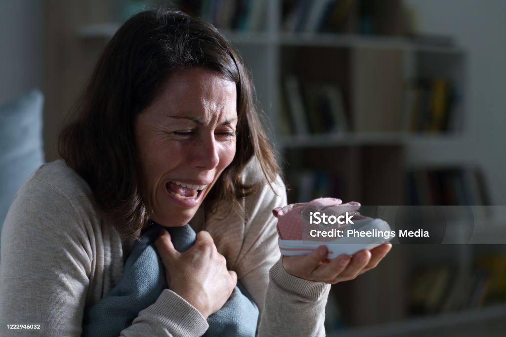 Sad mother missing her lost daughter at night at home Sad mother crying missing her lost baby daughter holding shoe sitting at night at home Child Stock Photo