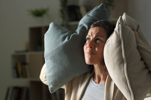 Annoyed adult woman suffering neighbour noise at night at home Annoyed adult woman suffering neighbour noise in the livingroom at night at home nettle stock pictures, royalty-free photos & images