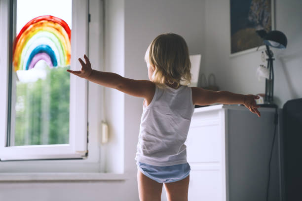 ragazza carina che si diverte a saltare sul letto sullo sfondo della finestra con un arcobaleno dipinto. - biancheria intima foto e immagini stock