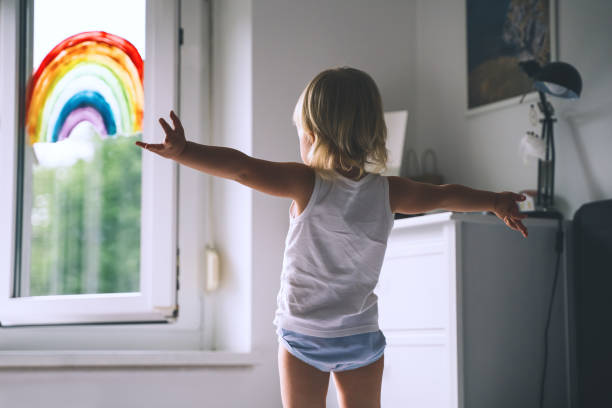 cute little girl having fun time jumping on bed on background of window with a painted rainbow. - roupa interior imagens e fotografias de stock