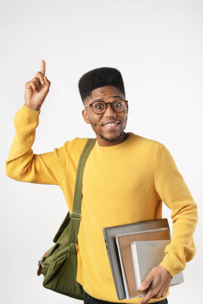 istock Vertical shot of student in eyeglasses with backpack holding laptop while pointing isolated on white background 1222953347