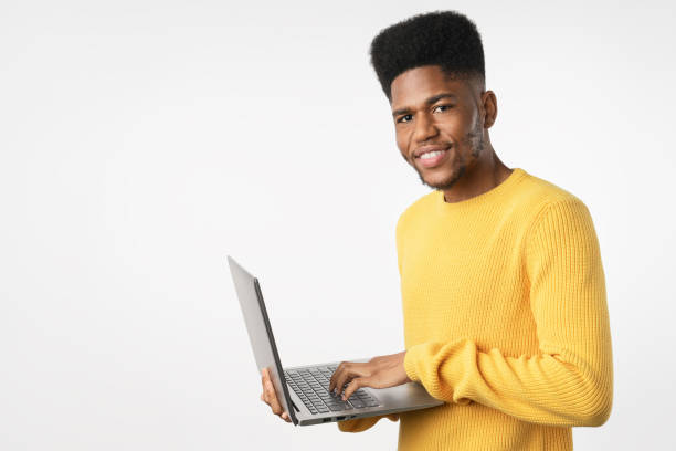 istock Young cheerful african man using laptop computer standing isolated over white background 1222953430