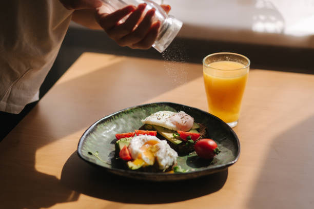 Delicious breakfast at home. Woman salt Sandwich with fresh sliced avocado above rye toasted bread with cherry tomatoes and poached egg on green plate. Fresh orange juice Yolk flows out on toast