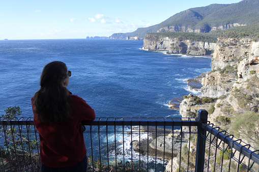 Silhouette of young adult woman looks at sea cliffs at Tasman National Park Tasman Peninsula Tasmania Australia