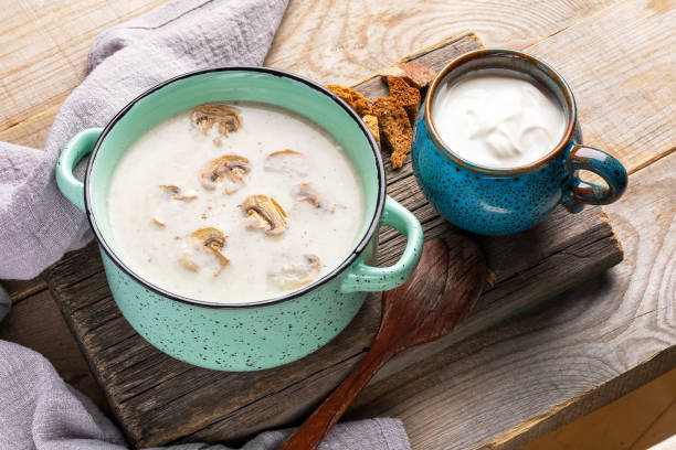 poêle en céramique turquoise avec soupe de crème de champignons, tasse avec crème sure et craquelins sur la vieille planche en bois sur fond rustique en bois. - food heat serving size casserole photos et images de collection