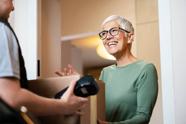 Senior woman received package from courier Senior woman received package from delivery person and paying during home isolation - quarantine caused coronavirus. customer experience stock pictures, royalty-free photos & images