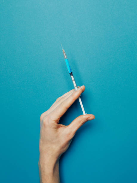 istock Hand holds syringe with experimental coronavirus vaccine on blue background, top view. Healthcare Medicine Vaccination Coronavirus Covid-19 Concept 1222961891