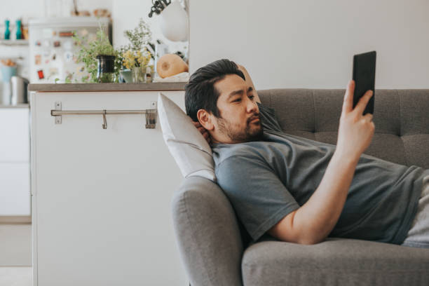 Asian man reads electronic book at home on the couch