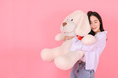 Portrait of beautiful asian girl with closed eyes hugging big white dog doll, isolated on pink background