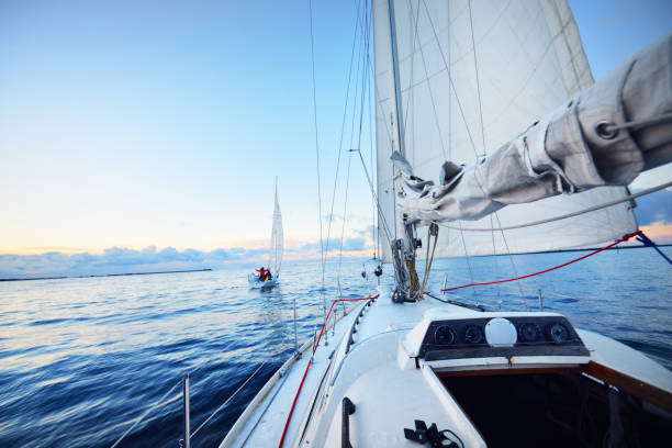 sloop aparejado yates navegando en un agua quieta al atardecer. escarcha y primera nieve en la cubierta, vista de cerca al arco, mástil, cuerdas y velas. cielo azul claro con coloridas nubes de invierno. noruega - clear sky water sports and fitness yacht fotografías e imágenes de stock