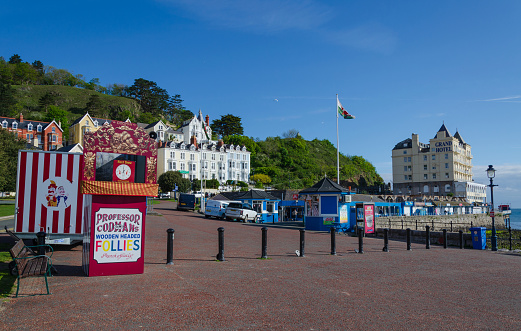 Llandudno, UK : May 6, 2019: A general scene of the promenade at Llandudno on a sunny morning with very few people. A traditional Punch & Judy stall is closed, awaiting the first show time.