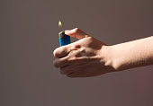 A woman holds a lighter with burning fire in the shade. Hands that are lighter on the gray background
