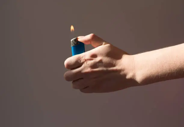 Photo of A woman holds a lighter with burning fire in the shade. Hands that are lighter on the gray background