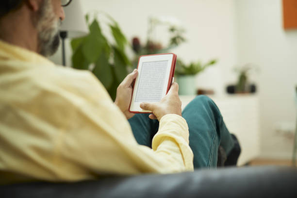 One mid adult man reading on an e-reader seen from behind.