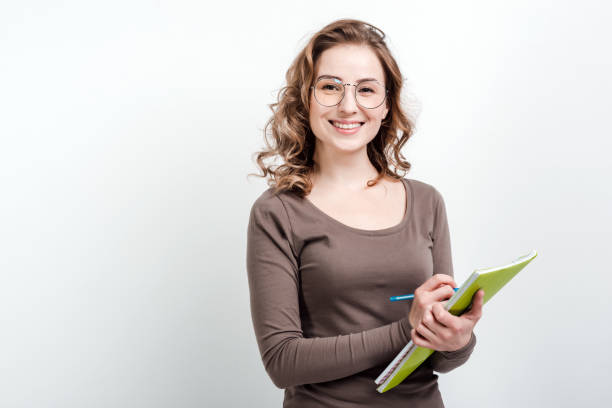 istock Attractive girl in glasses makes notes in exercise book on a white background 1222999787