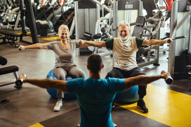 istock Senior couple exercising with personal trainer using dumbbells at the gym 1223003129