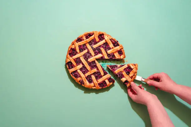 Above view with a woman's hands grabbing a slice of blueberries tart. Delicious homemade pie with a lattice crust and blueberries filling