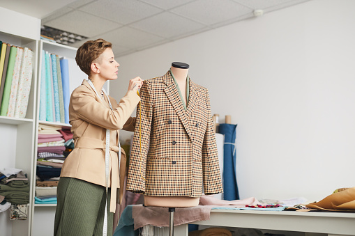 Young tailor taking measurements from jacket on mannequin while working in the workshop