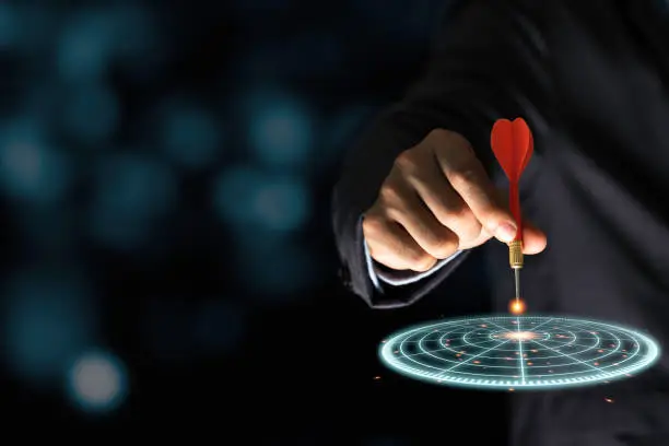 Photo of Businessman throwing red arrow dart to virtual target dart board. Setup objectives and target for business investment concept.