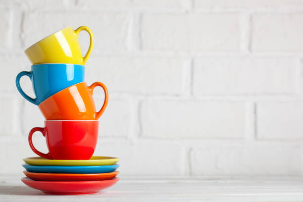 Colorful cups on the white background of a brick wall. Background with copy space. Selective focus.