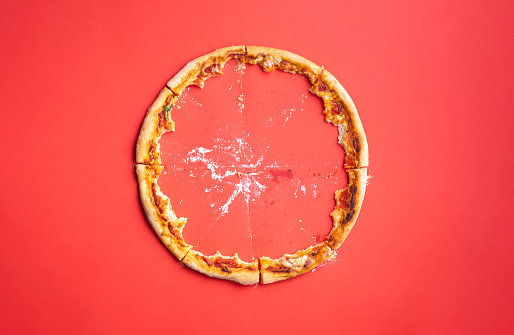 Pizza leftovers on a red background, above view. Pizza crust only. Eaten pizza.