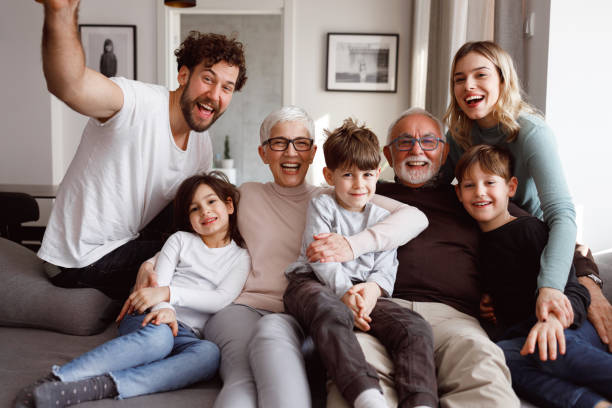 Big family A multi-generational family is posting in front of the camera. They are sitting on the sofa in the living room. social gathering photos stock pictures, royalty-free photos & images