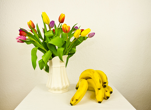 A light still life with a bouquet of colourful tulips an fruits, a melon and bananas