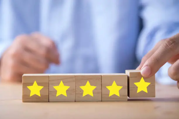 Photo of Businessman hand putting yellow star which is printed on wooden cube. Customer evaluation survey and satisfaction concept.