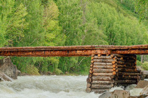 Wooden bridge of logs on mountain river. Crossing for pedestrians over fast creek