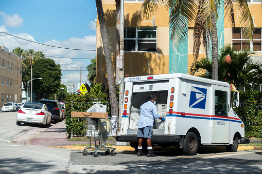 Miami Beach, FL, United States - May 4, 2020 - A postal worker sorts mail with a protective face mask and gloves during the Coronavirus pandemic.