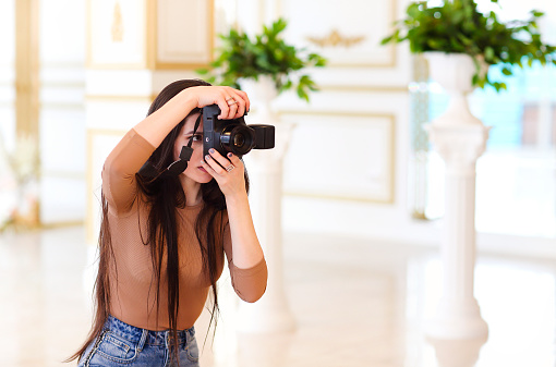 Modern female photographer with photo camera taking pictures of interior while standing in light vintage room