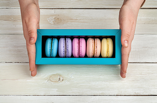 Female hands holding box with macaroons on wooden background