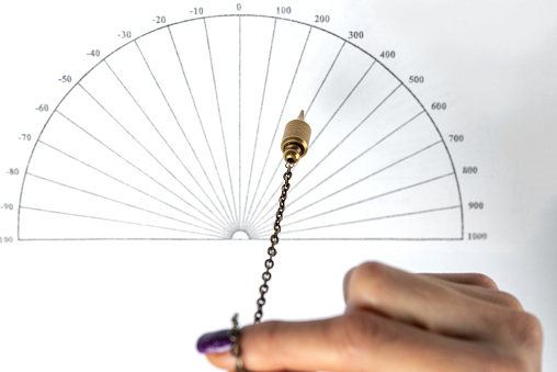 Arm of a dowser with hand-held pendulum over the chart. Selective focus.