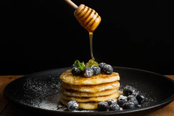 Dipping honey with a dipper on pancakes with blueberries and icing sugar