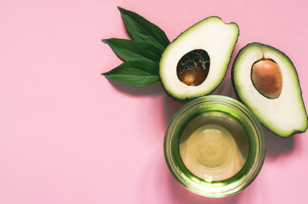 Beauty theme. Skin care concept. Avocado with green leaves. Two halves of avocado and avocado oil in a bowl on a pink background. two objects vegetable seed ripe stock pictures, royalty-free photos & images