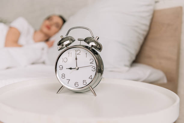 istock selective focus of vintage alarm clock on bedside table and sleeping woman on background 1223018164