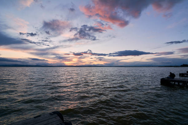 Landscape of a lake with storm clouds, moving waters reeds in the water, bluish tones, pier