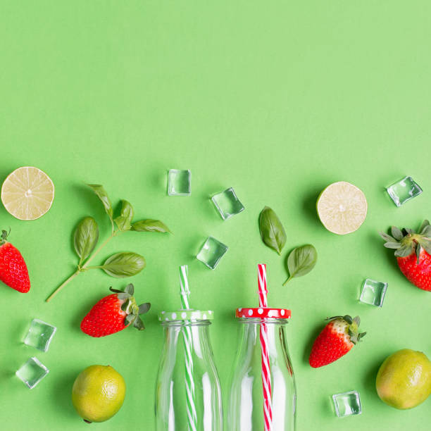 flat lay com ingredientes para a bebida refrescante de verão ou smoothie, cubos de gelo, ervas e potes de vidro em fundo verde, vista superior, banner web. morango, limão, gelo e manjericão para coquetel de verão - strawberry mocktail smoothie cocktail - fotografias e filmes do acervo