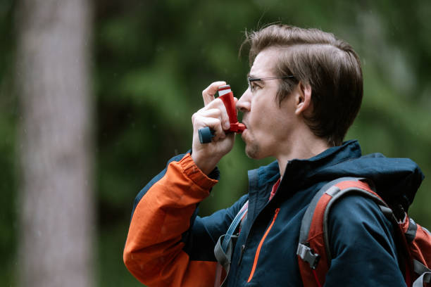 Man Using Inhaler While Hiking Outdoors A young man enjoying a nature hike uses his inhaler to help manage symptoms of asthma or cystic fibrosis. asthmatic photos stock pictures, royalty-free photos & images