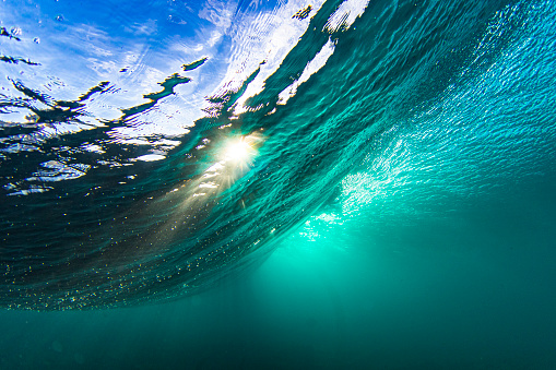 Light rays from the sun penetrating through a wave in a clear blue underwater scene.