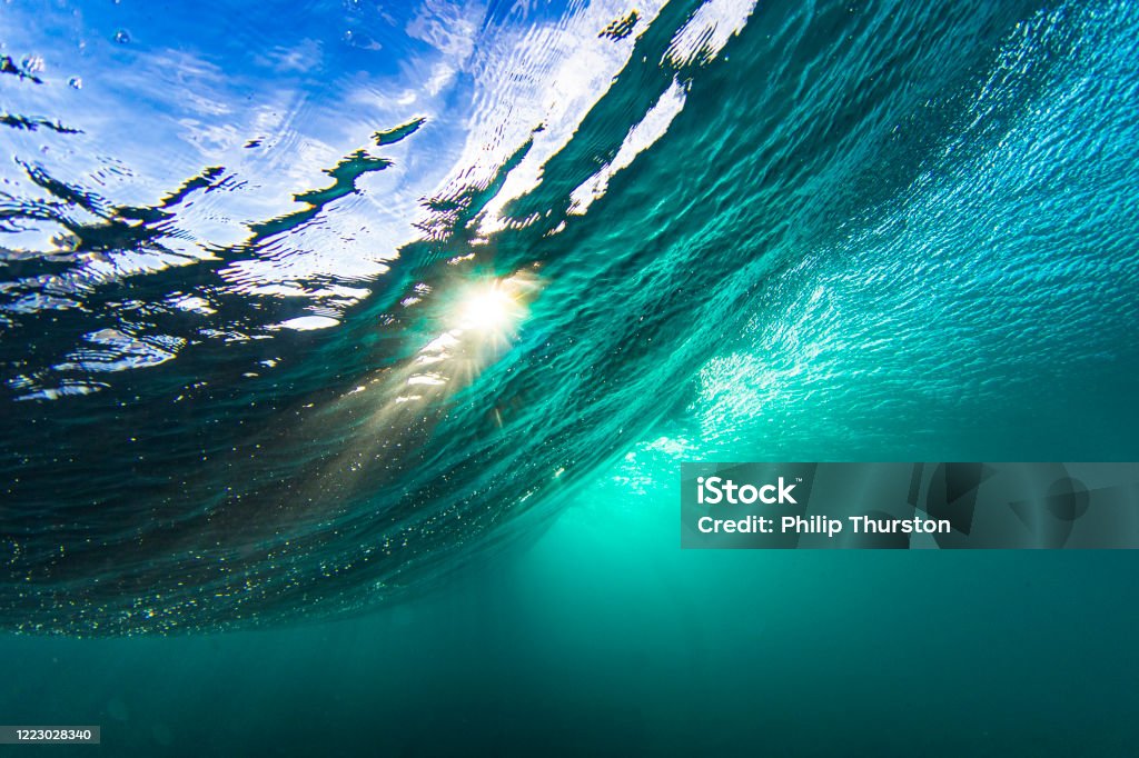 Light rays from the sun penetrating through a wave in a clear blue underwater scene Light rays from the sun penetrating through a wave in a clear blue underwater scene. Sea Stock Photo