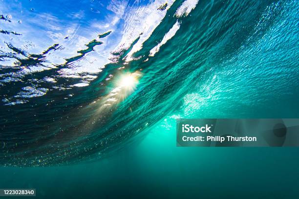 Light Rays From The Sun Penetrating Through A Wave In A Clear Blue Underwater Scene Stock Photo - Download Image Now