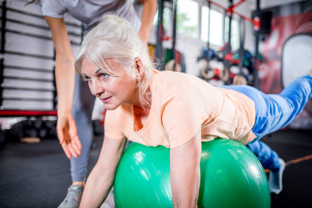 seniorin mit trainer macht reha mit pilates ball im rehabilitationszentrum - physical therapy exercise machine exercising exercise equipment stock-fotos und bilder