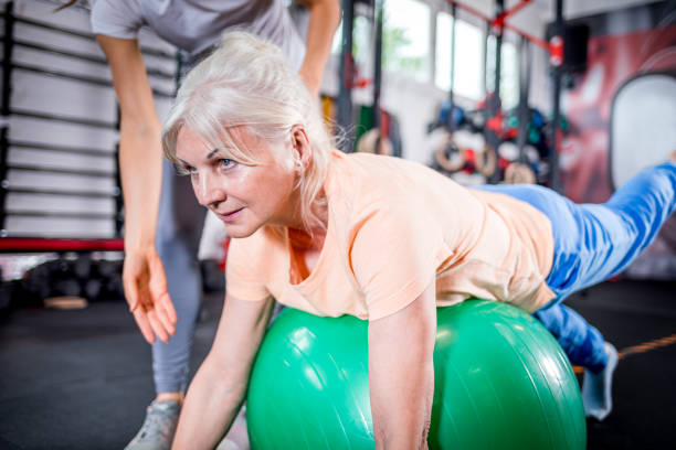 mujer mayor con entrenador haciendo rehabilitación usando pilates bola en el centro de rehabilitación - pilates health club gym exercising fotografías e imágenes de stock