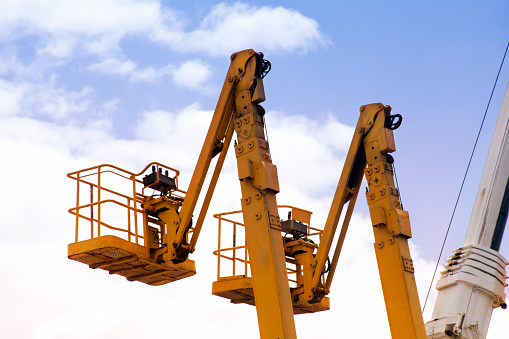 Two tall yellow cherry pickers, sky background. Construction equipment.