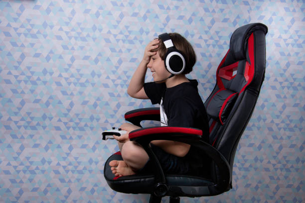 garçon s’asseyant dans la chaise de joueur avec le casque et le contrôle de jeu vidéo - video game joystick leisure games control photos et images de collection