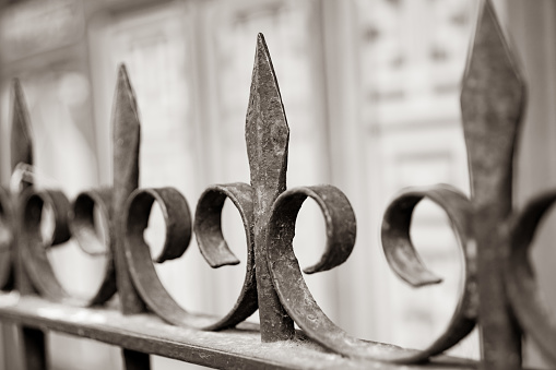 Wrought iron fence spikes and decorative curl shapes close up in selective focus. in monochrome.