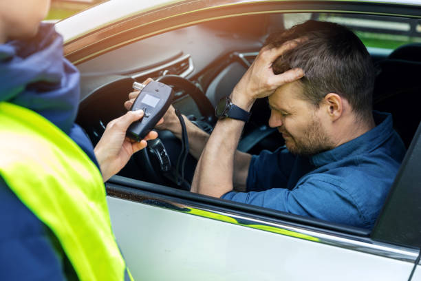 drink and drive concept - sad drunk man sitting in the car after police alcohol test with alcometer stock photo