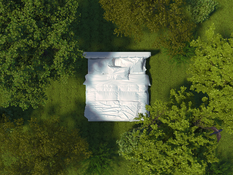A bed with white linens stands on the grass in the forest among the trees. White bed outdoors surrounded by a landscape in a top view. Creative conceptual illustration. 3D rendering.
