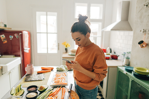 Photo of a young woman checking sushi recipes online in the kitchen of her apartment.